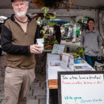 Jim Proust holds red pine and red oak seedlings he received at Ecology Ottawa tree giveaway booth at the Elgin Street Market on September 4, 2022. Volunteer Kristin Stock-Still is at the booth. (Arno Ryser/The BUZZ)